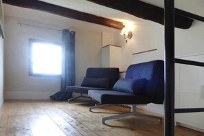 A room with a wooden floor, two dark-colored chairs, a window with curtains, and a wall-mounted light fixture. - Relaxing Home Near Pool in Malaucène (Malaucène)