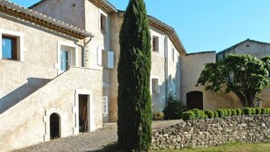 A traditional building with a stone wall, a tall cypress tree, and a well-maintained lawn. - Relaxing Home Near Pool in Malaucène (Malaucène)