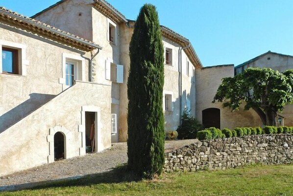 A traditional building with a stone wall, a tall cypress tree, and a well-maintained lawn.