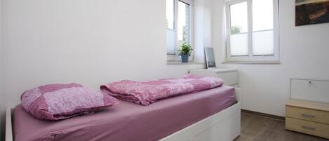 A bedroom with a single bed, a bedside table, a window, and a small cabinet.