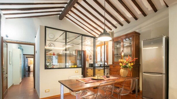 Une cuisine avec une table en bois, des chaises, un réfrigérateur et un luminaire suspendu.