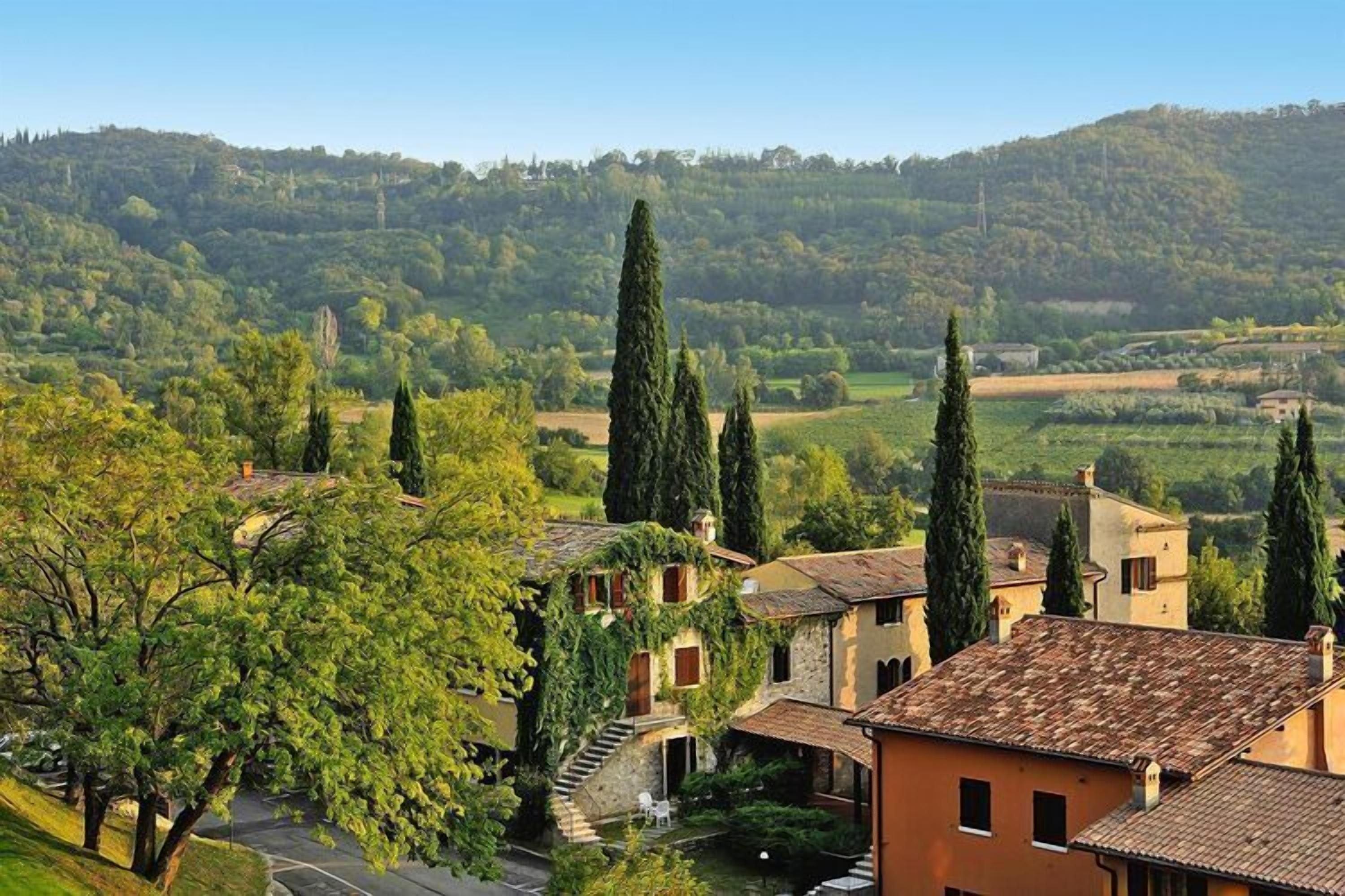 Un village rural avec des bâtiments traditionnels en pierre, une route sinueuse et une colline en arrière-plan.