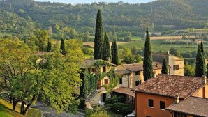 A rural village with traditional stone buildings, a winding road, and a hill in the background. - Apartments Poiano in Garda with pool (Garda)