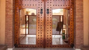 Un'ampia porta doppia in legno con un cancello in metallo, un lanterne appesa e un pavimento piastrellato.