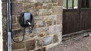 Edificio de piedra con un muro de ladrillo, una ventana y una estación de carga para vehículos eléctricos.