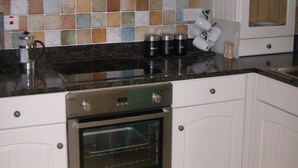Una cocina con armarios blancos, salpicadero de azulejos, campana extractora de acero inoxidable y horno empotrado.