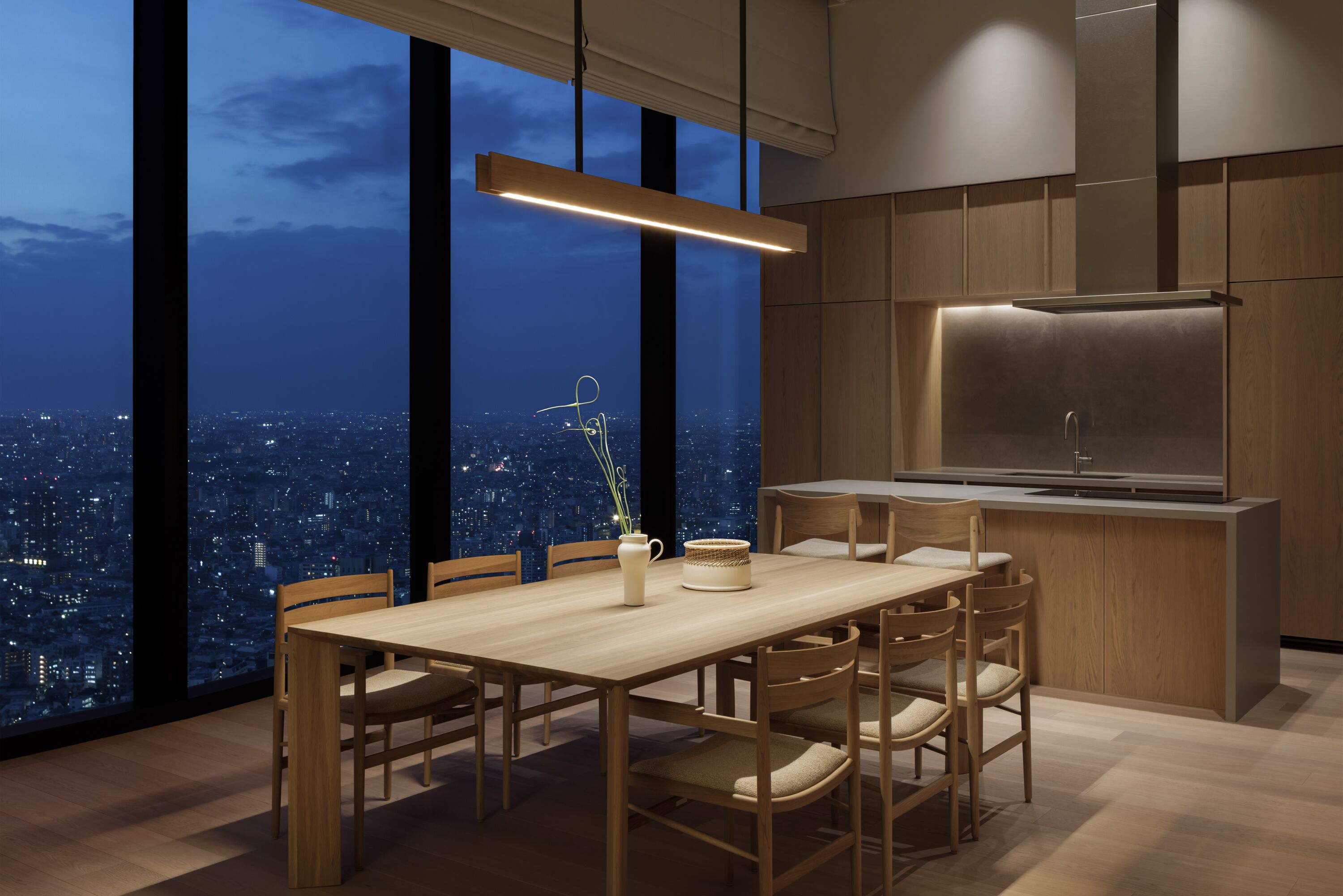 A modern kitchen with a large island, wooden cabinetry, and a city view through large windows.