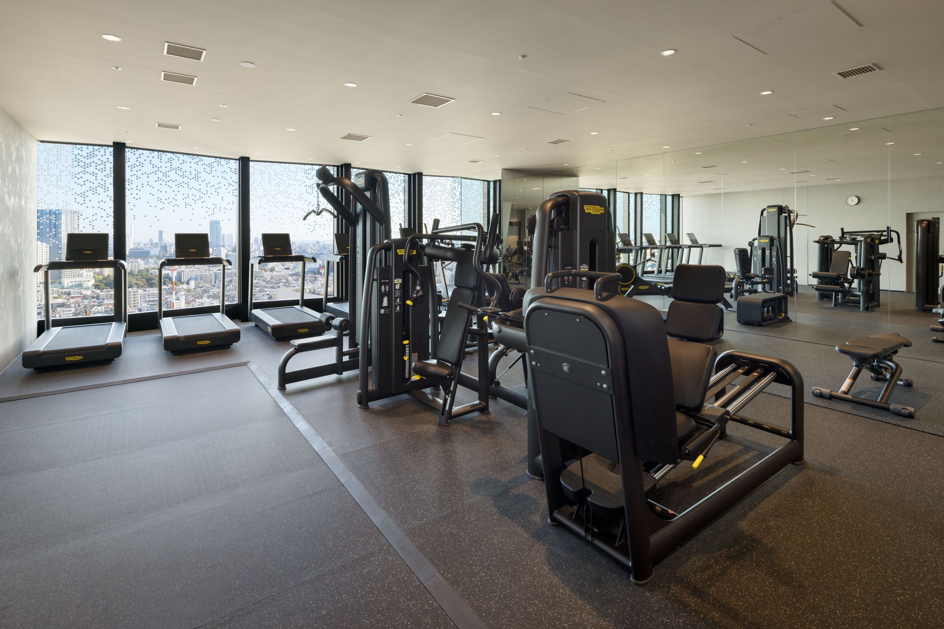 A modern gym with treadmills, weight machines, and a large window offering a city view.