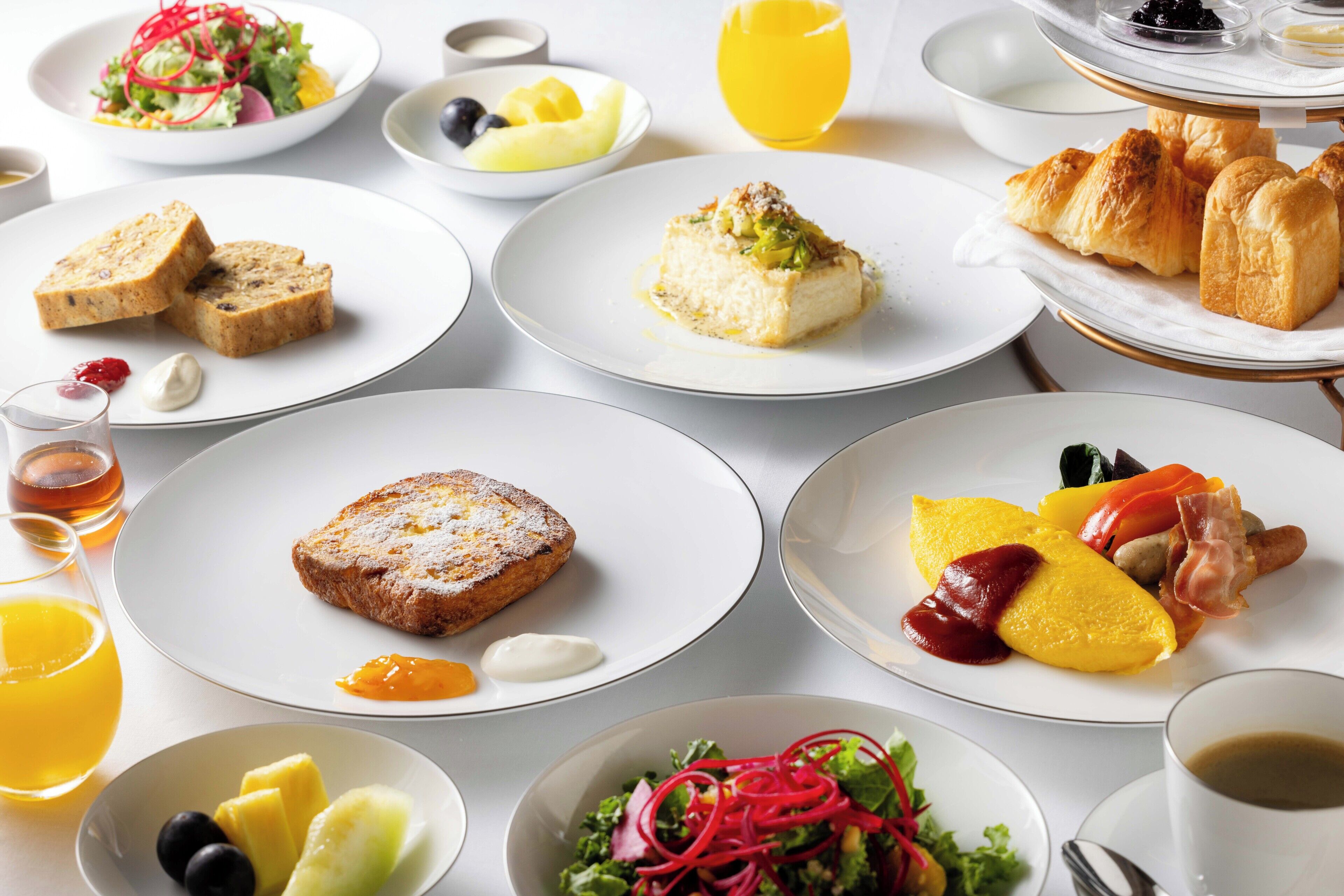 A breakfast buffet with various dishes including toast, omelette, croissants, and fruit.