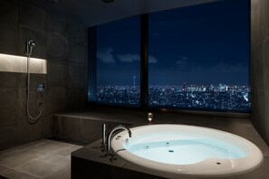 A modern bathroom with a large bathtub, a shower, and a cityscape view through a large window.