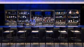 A bar with multiple shelves of bottles and glasses, and several bar stools.