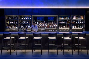 A bar with multiple shelves of bottles and glasses, and several bar stools.
