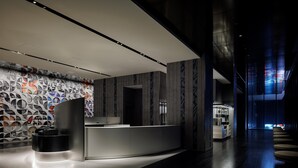 A modern reception area with a counter, a wall with circular patterns, and a staircase leading to upper floors. - HOTEL GROOVE SHINJUKU, A PARKROYAL Hotel (Tokyo)