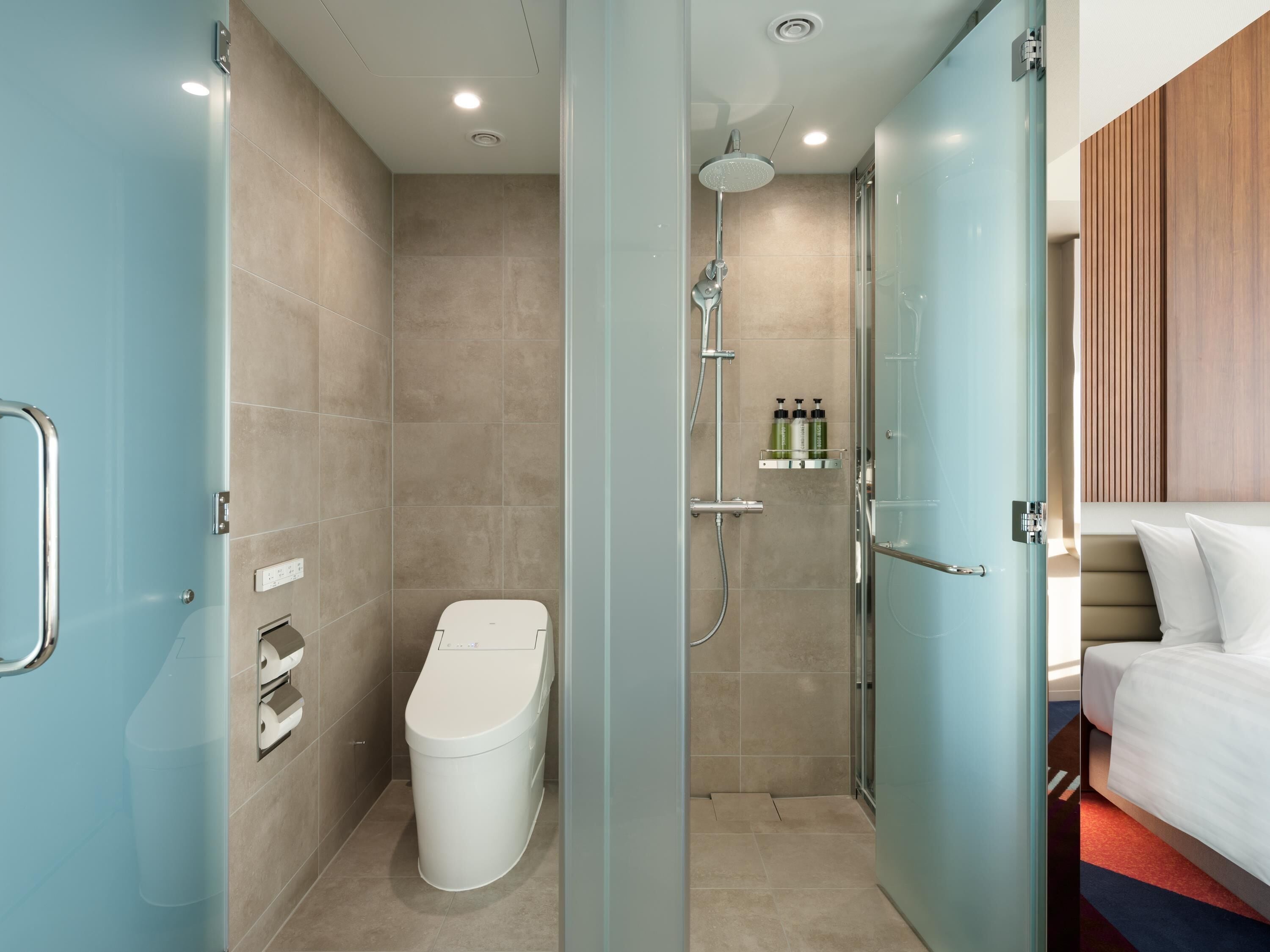Un baño moderno con ducha de vidrio, inodoro y mesita de noche con artículos de aseo.