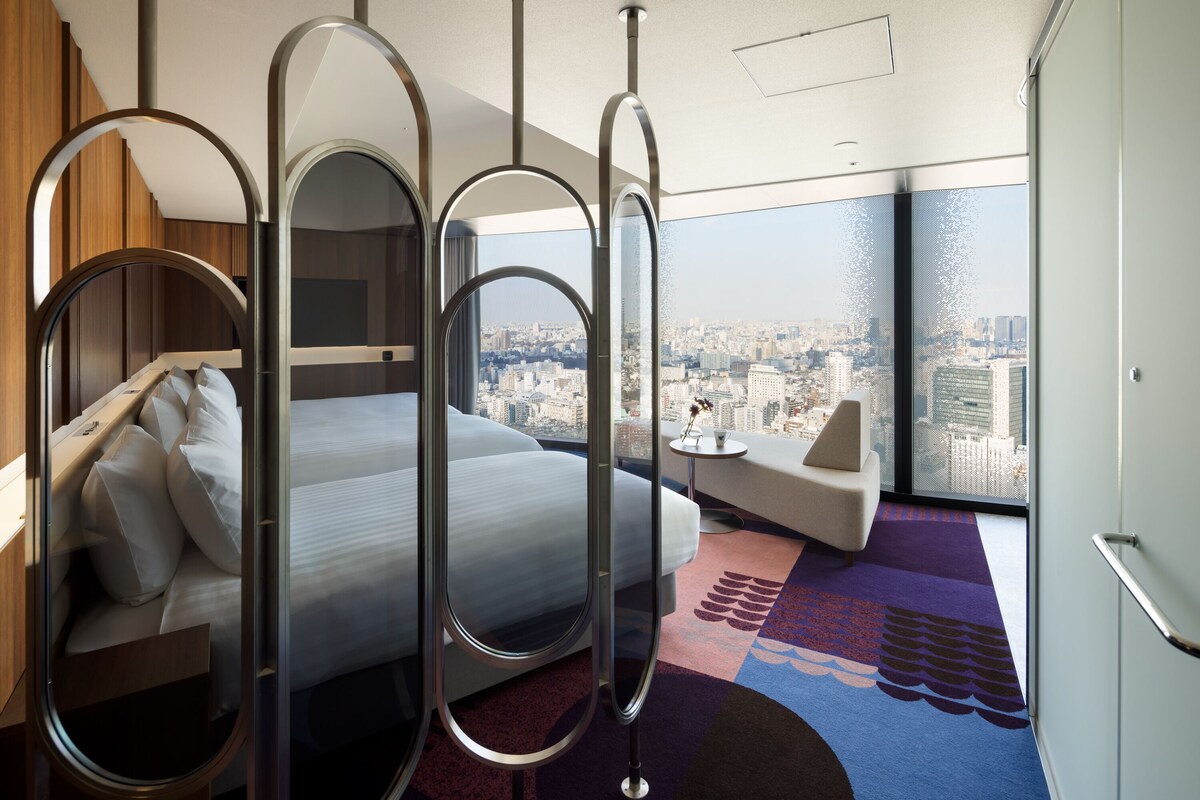 A modern hotel room with a bed, a sofa, and a city view.