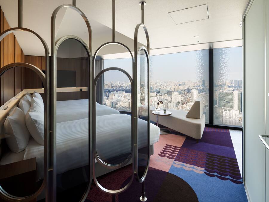 A modern hotel room with a bed, a sofa, and a city view.