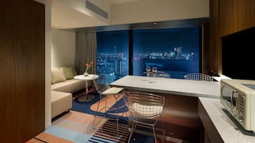 Una habitación de hotel moderna con vista a la ciudad, un sofá, un comedor y un televisor.