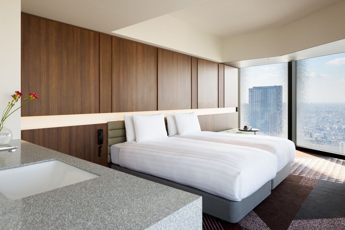 A modern hotel room with a large bed, a built-in desk, and a city view.