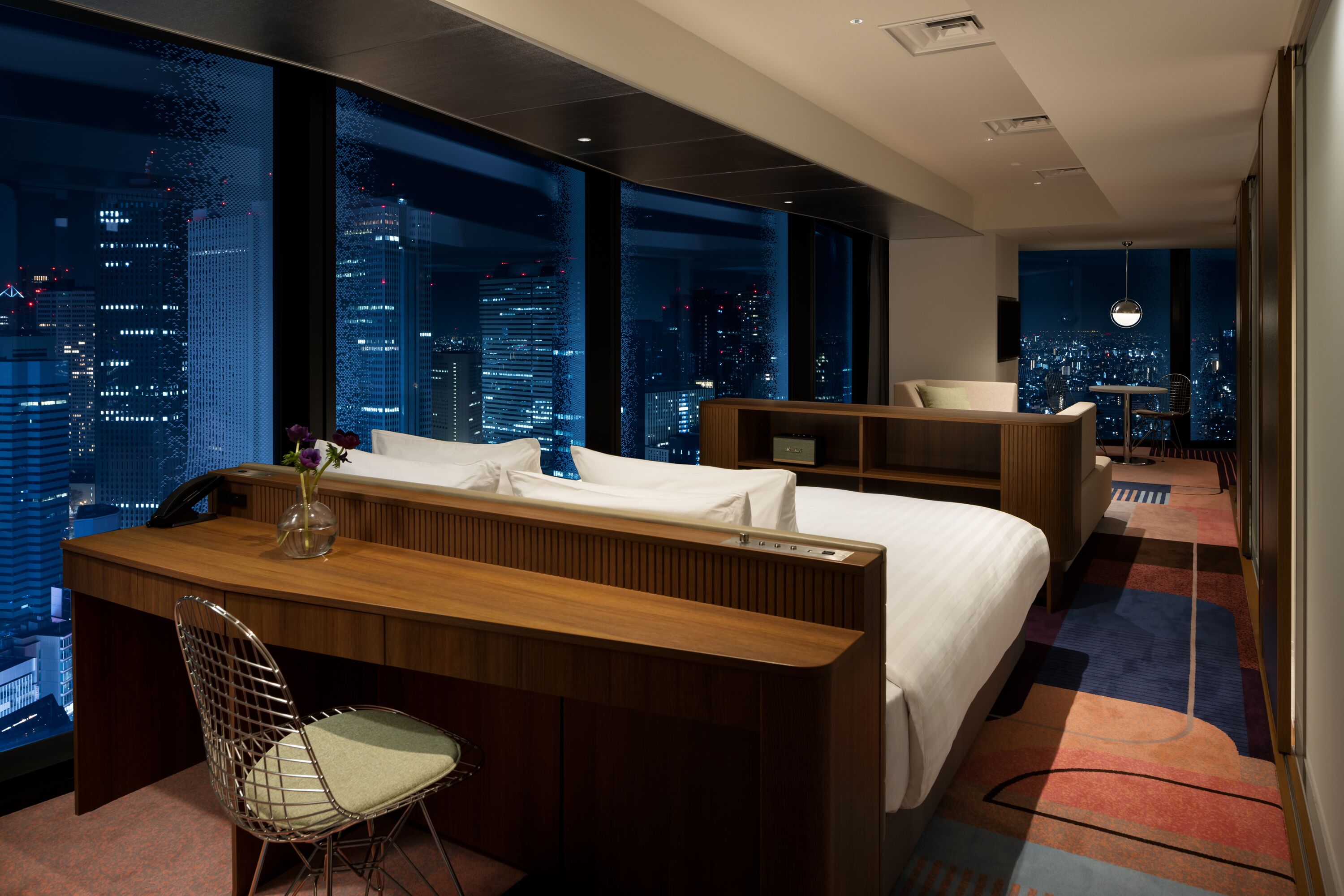 A modern hotel room with a city view, a desk, a bed, and a seating area.
