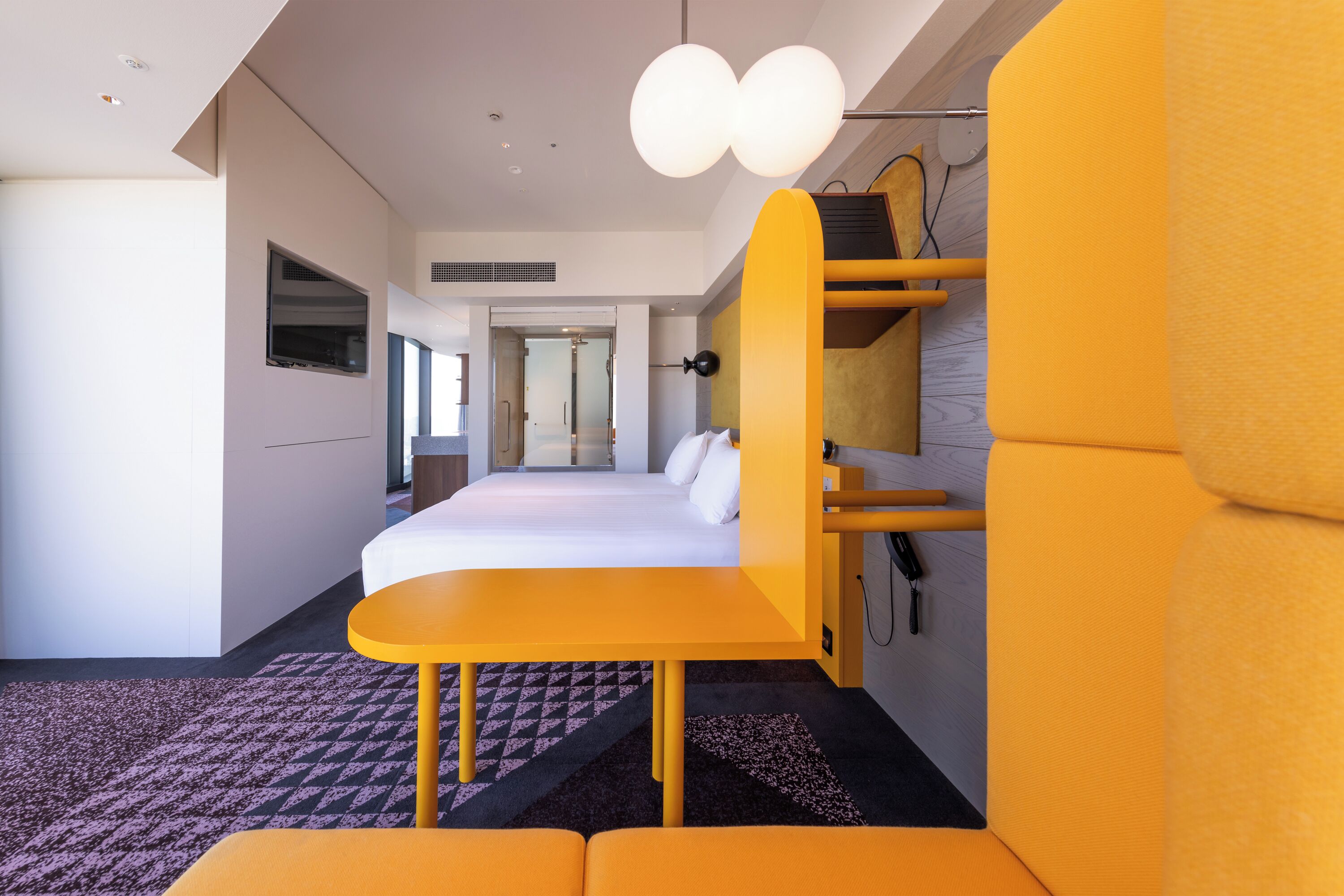 A modern hotel room with a bed, a desk, and a seating area.