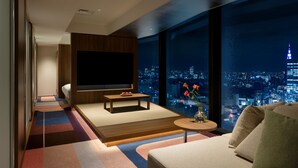 A modern hotel room with a large TV, a sofa, a small coffee table, and a view of a cityscape at night. - HOTEL GROOVE SHINJUKU, A PARKROYAL Hotel (Tokyo)