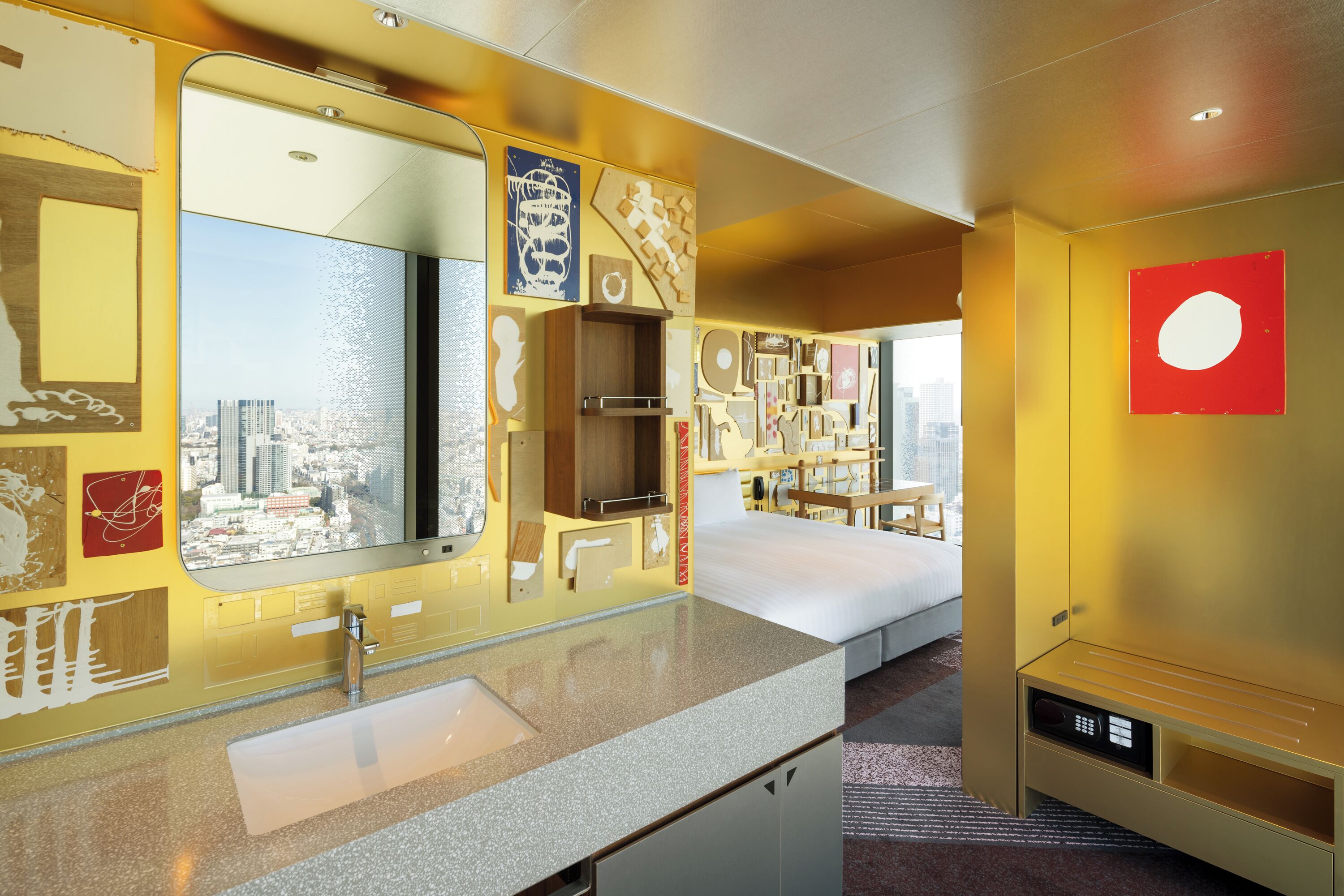 Habitación de hotel con un espejo grande, una cama, tocador con lavamanos y vistas a la ciudad.