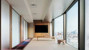 A modern hotel room with a large window, a flat-screen TV, a wooden bench, and a small table with a vase. - HOTEL GROOVE SHINJUKU, A PARKROYAL Hotel (Tokyo)