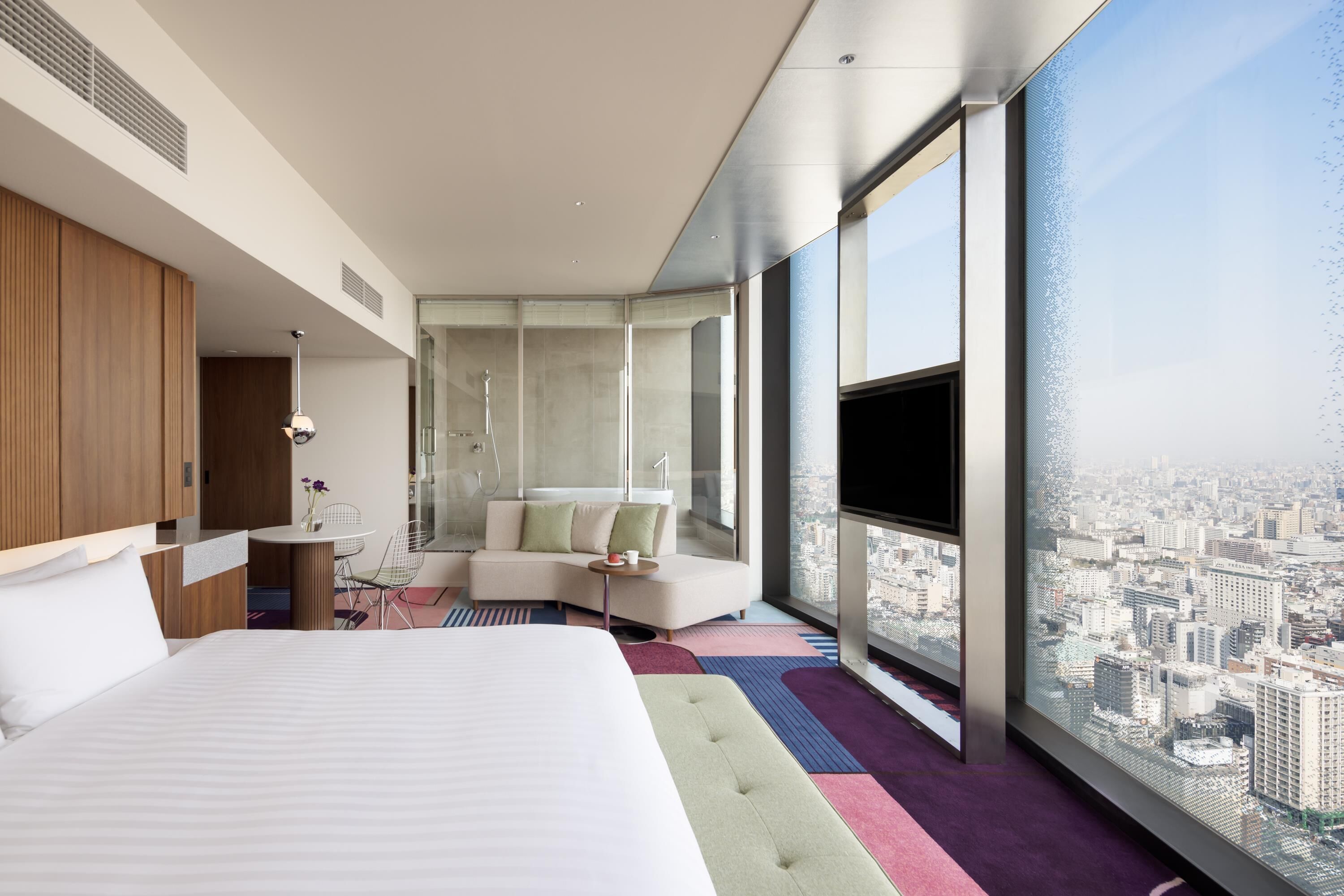 A modern hotel room with a large bed, a seating area, a bathroom, and a city view.