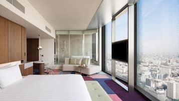 A modern hotel room with a large bed, a seating area, a bathroom, and a city view.