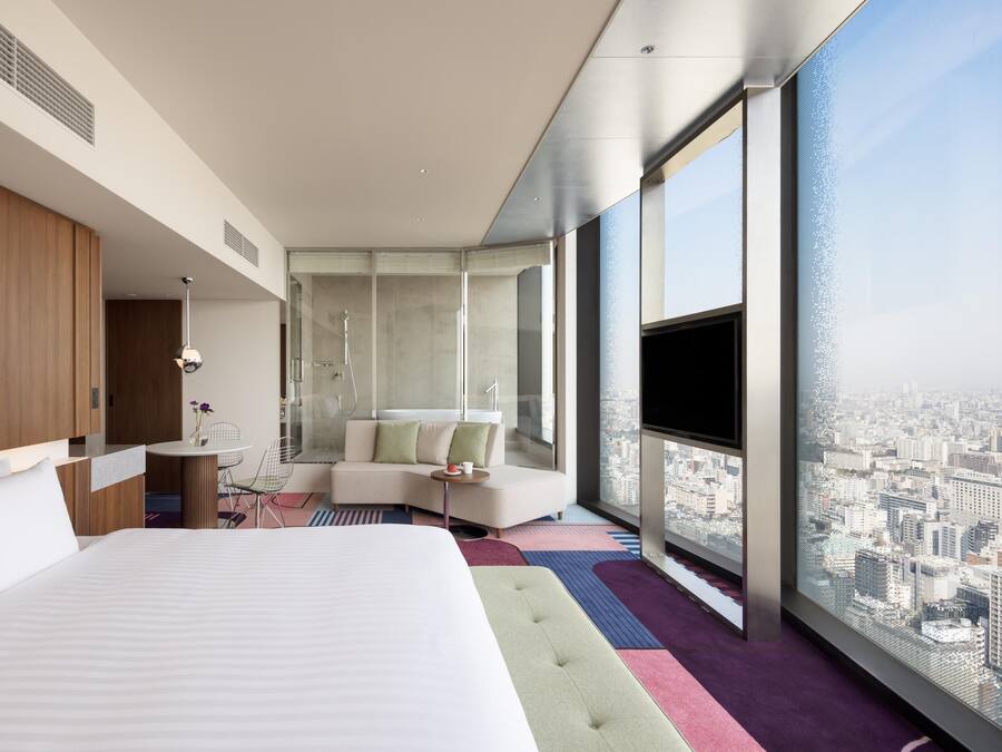 A modern hotel room with a large bed, a seating area, a bathroom, and a city view.