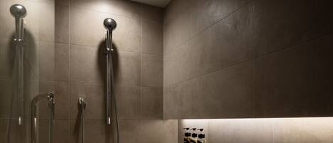 Une salle de bain moderne dotée de deux pommes de douche, d’une étagère intégrée pour les articles de toilette et d’un luminaire au plafond.