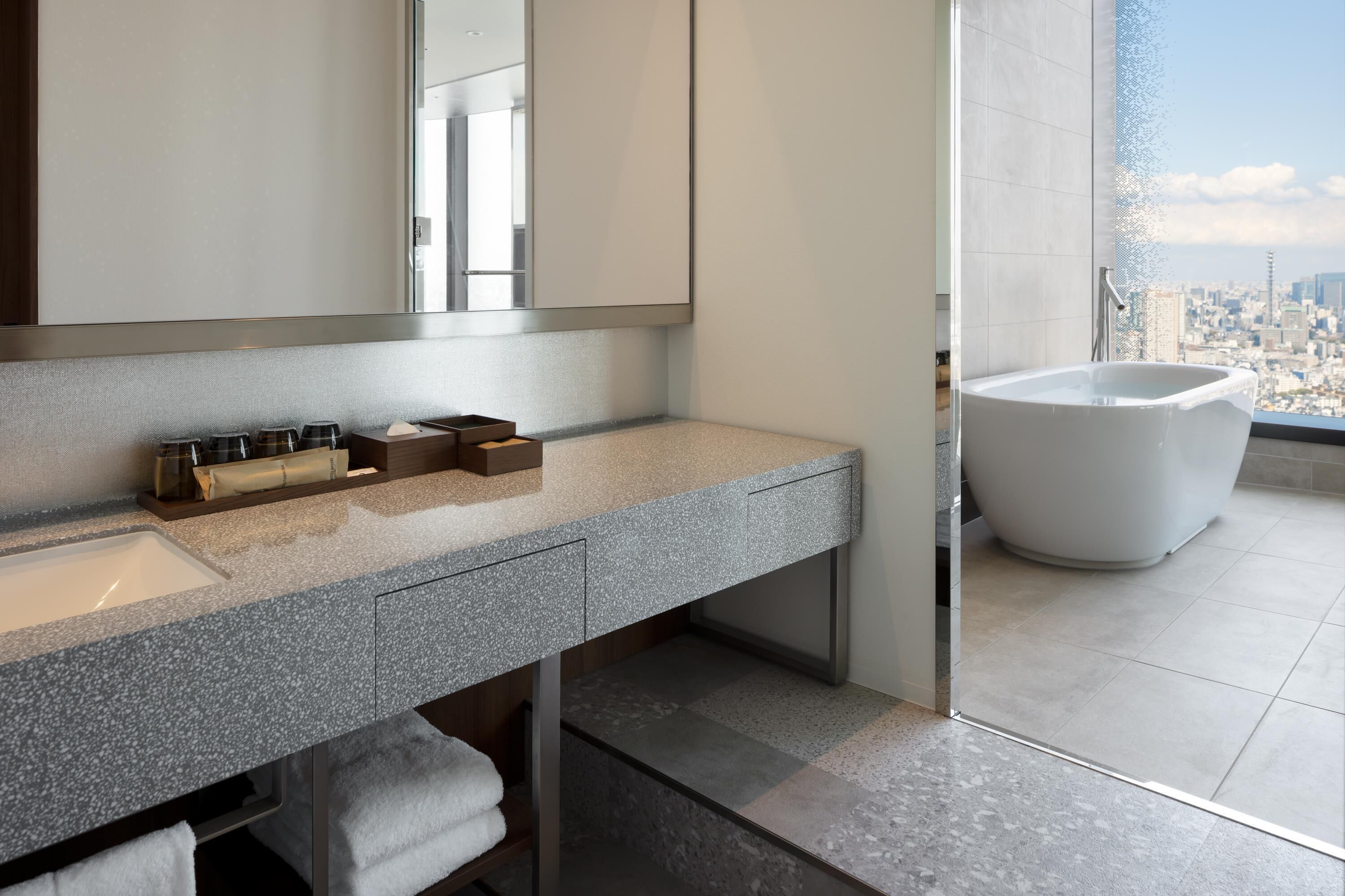 A modern bathroom with a granite countertop, a large mirror, and a freestanding bathtub.