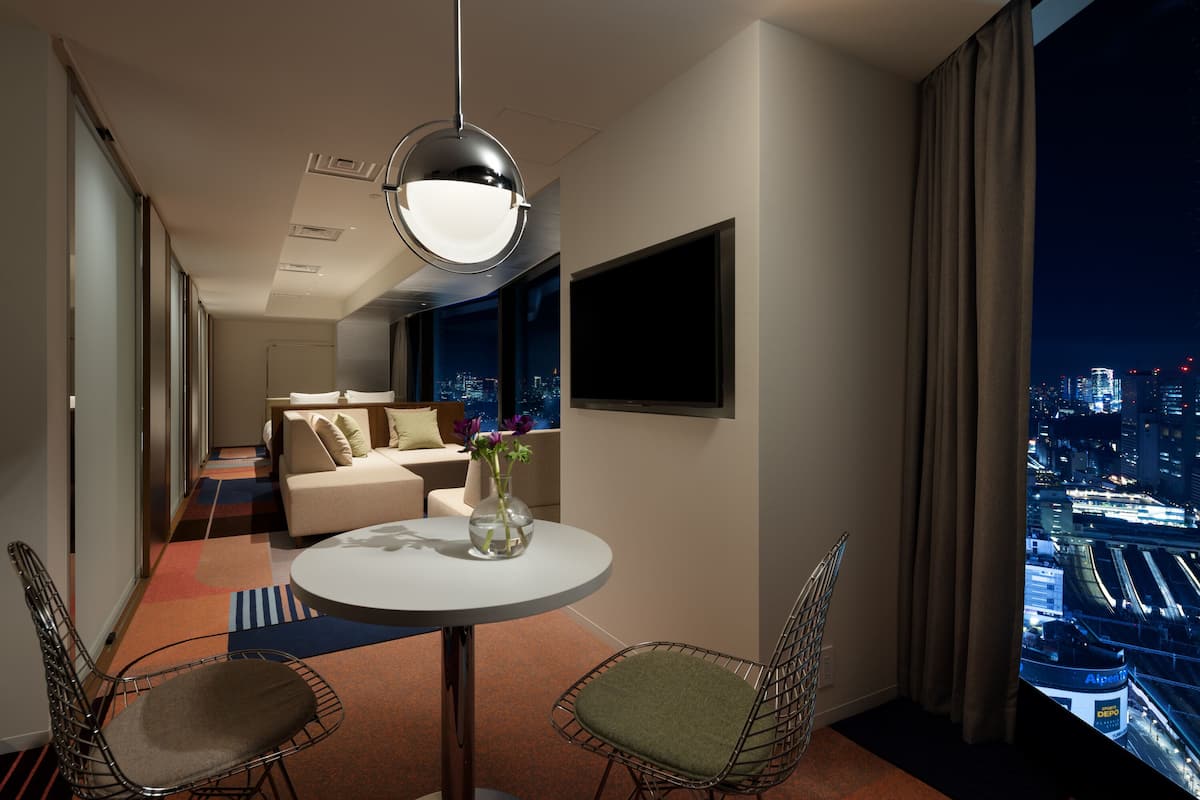 Ett modernt hotellrum med utsikt över staden, ett runt matbord, två stolar, en soffa och ett stort fönster.