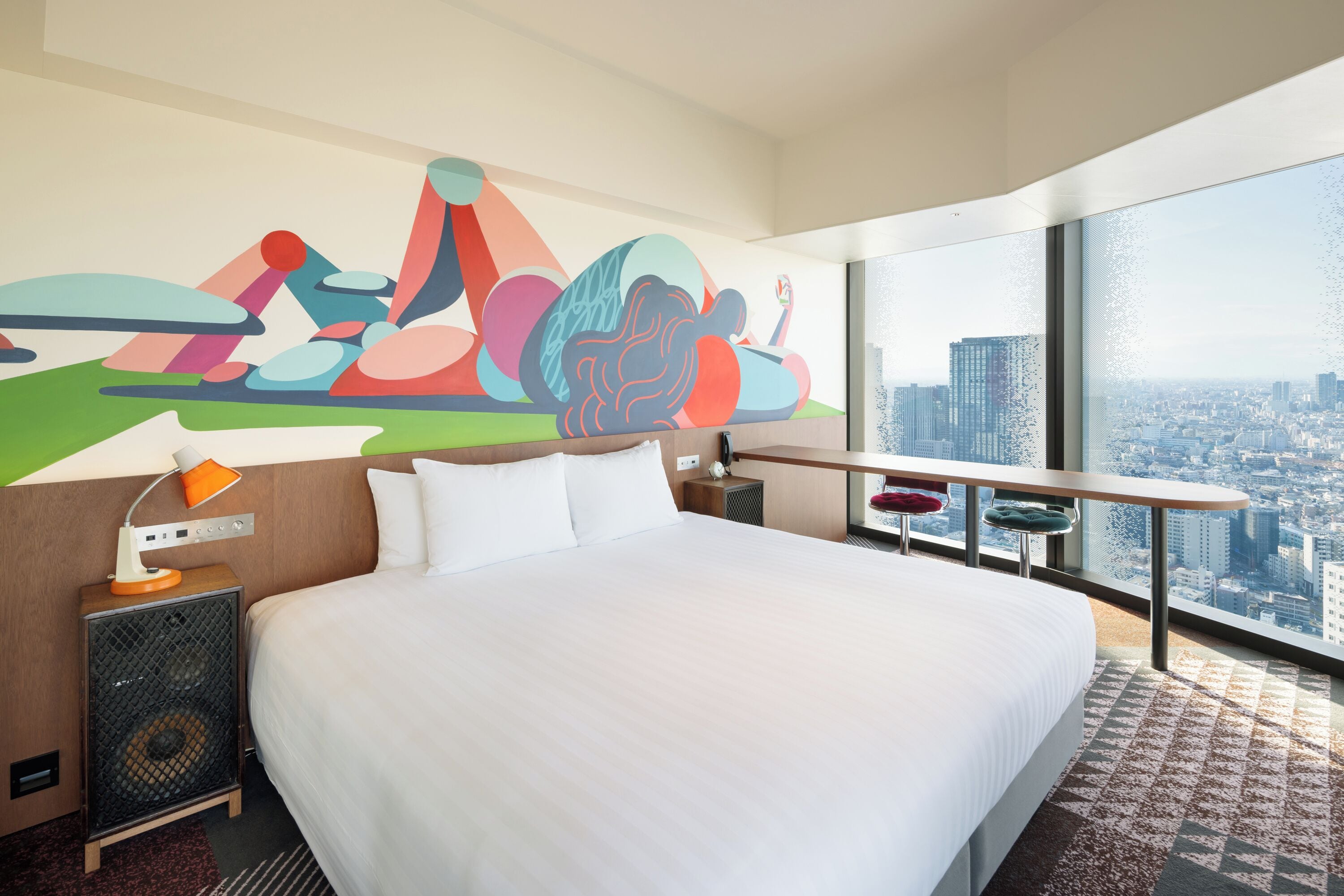 A hotel room with a large bed, a city view, a colorful abstract mural, and a modern design.