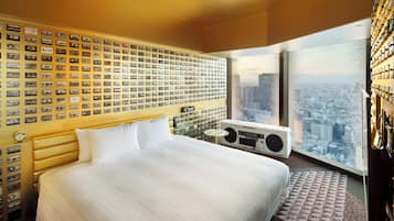 Une chambre d’hôtel avec un grand lit, un mur recouvert de cassettes audio, une radio et une vue sur la ville.