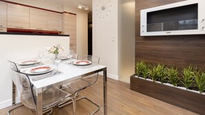 Un comedor moderno con una mesa blanca preparada para cuatro personas, sillas transparentes, un televisor empotrado en la pared y un jardín vertical con plantas.