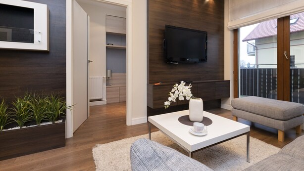 Una sala de estar moderna con un televisor de pantalla plana, una mesa de centro blanca, un sofá gris y piso de madera.