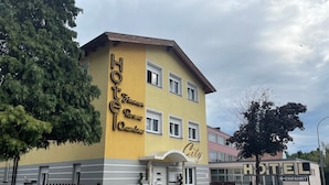 A hotel with a yellow facade, a sign reading "Hotel Zimmer Ross Chambers City," and a directional sign pointing to "Einfahrt."