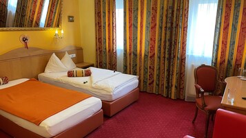 Quarto de hotel com duas camas, uma escrivaninha, uma cadeira e um espelho.