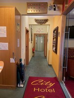 Corredor de hotel com tapete vermelho, portas de madeira, um extintor de incêndio e uma placa indicando o Hotel City.