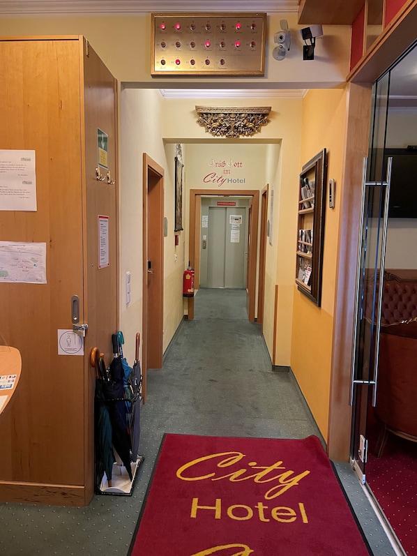 Pasillo de hotel con alfombra roja, puertas de madera, un extintor y un cartel que indica Hotel City.