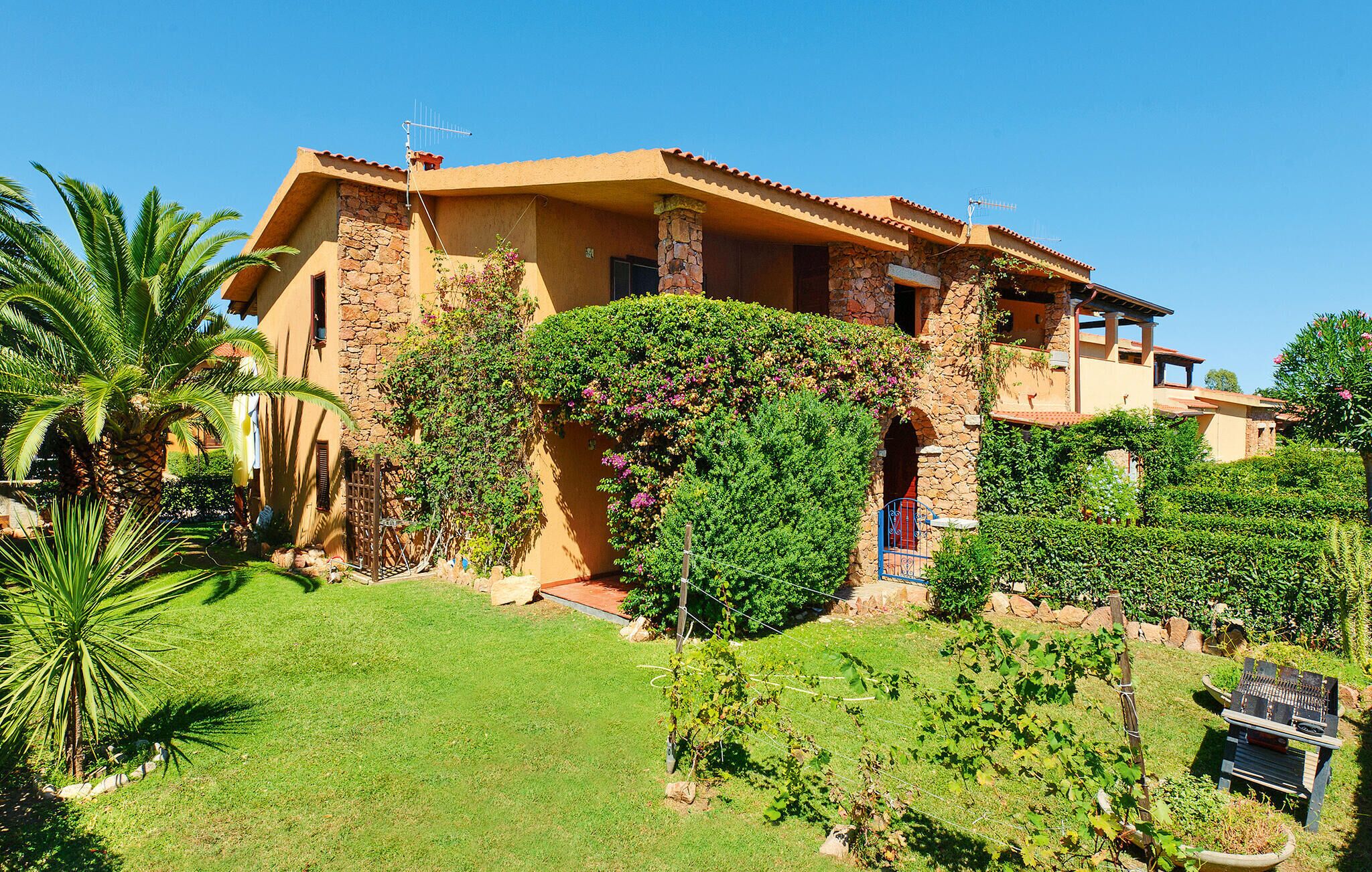 A two-story house with stone and stucco exterior walls, a stone staircase, and a well-maintained garden with palm trees and grapevines.