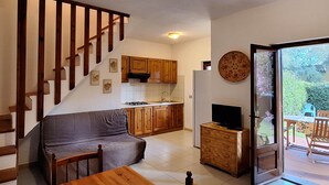 A compact living space with a sofa, wooden dining table, kitchen area, and a sliding glass door leading to an outdoor patio.