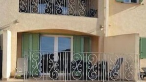 Un edificio a due piani con un balcone al piano superiore, gradini in pietra che conducono all'ingresso e un muro in pietra decorato con vasi di piante.