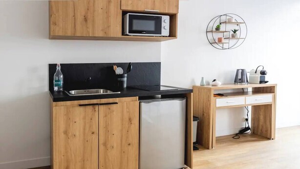Eine kleine Küche mit Holzausstattung, einem eingebauten Mikrowellenherd, einem Kühlschrank und einem kleinen Schreibtisch mit Schubladen.
