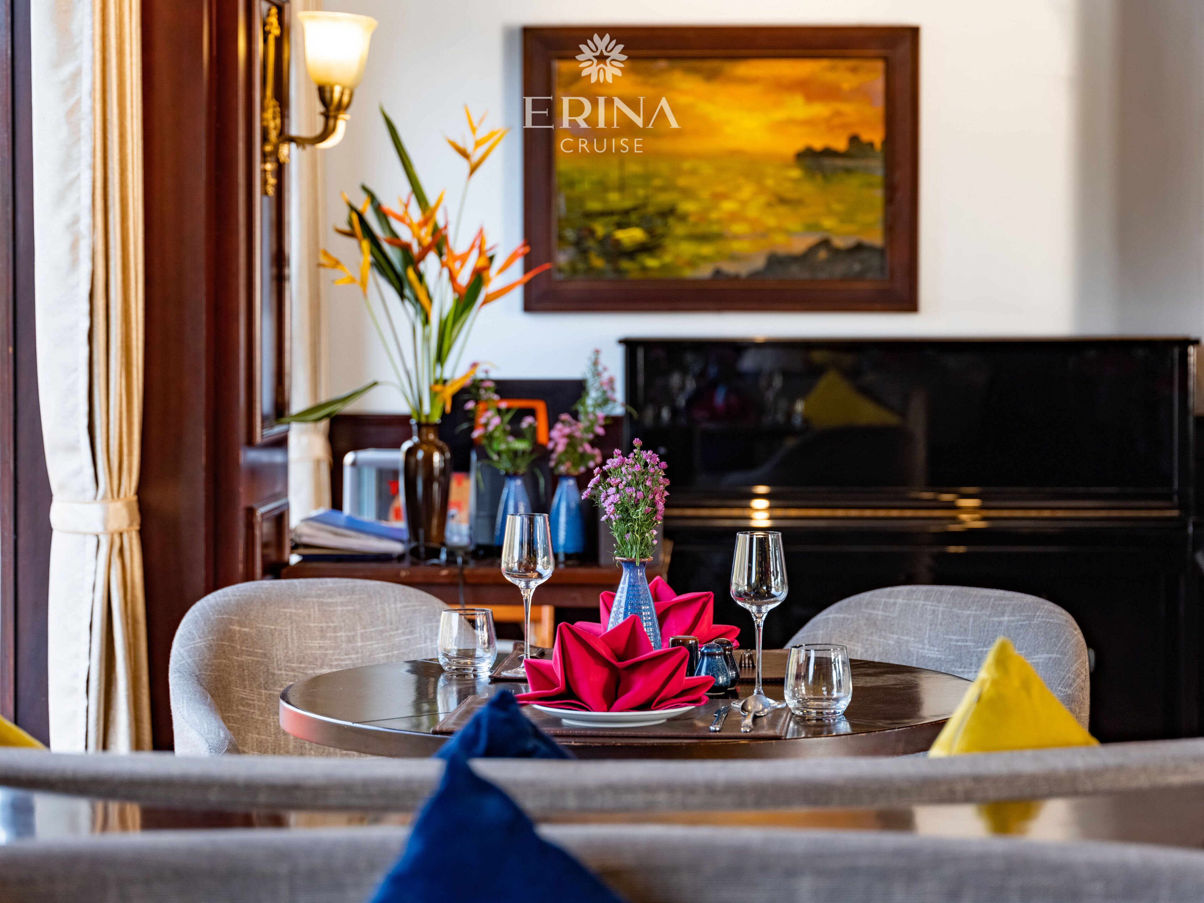 Un coin repas avec une table dressée pour deux personnes, un téléviseur en arrière-plan et un tableau accroché au mur.