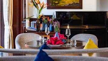 Un coin repas avec une table dressée pour deux personnes, un téléviseur en arrière-plan et un tableau accroché au mur.
