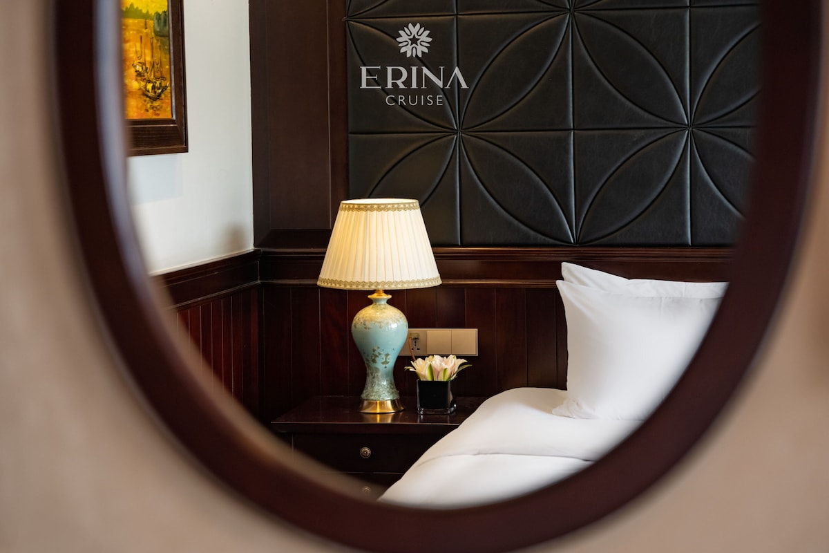 Et hotelværelse med en seng, et natbord, en lampe og en væg med teksten 'ERINA CRUISE'.