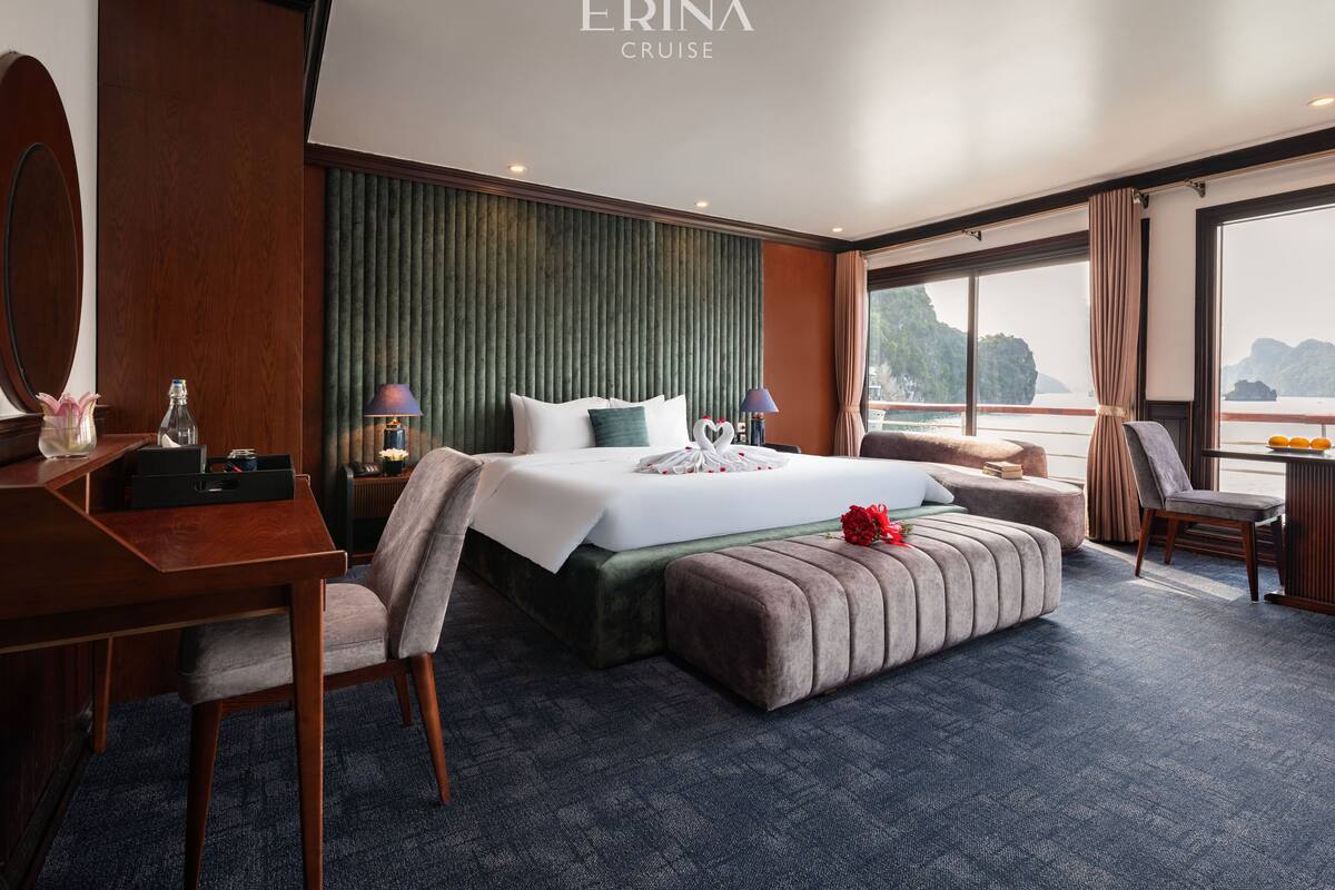 A hotel room with a large bed, a desk, a chair, a small table, and a view of the sea.