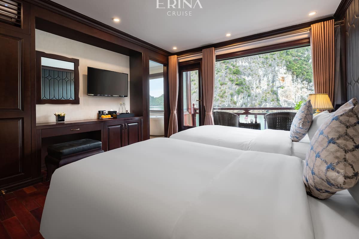 A hotel room with two beds, a TV, a desk with a chair, and a window with curtains.